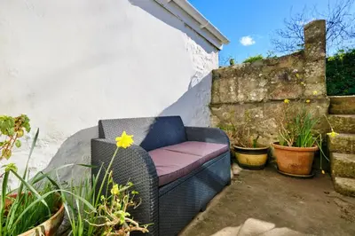 a wicker chair with a pink seat sitting on a patio at Finest Retreats - West Cottage at Goldsithney in Perranuthnoe
