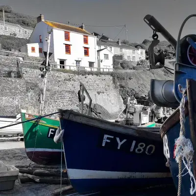 a blue boat sitting on the shore with a house in the background at Unique Retreat - 2 bedroom cliff top cottage with large terrace in Portloe