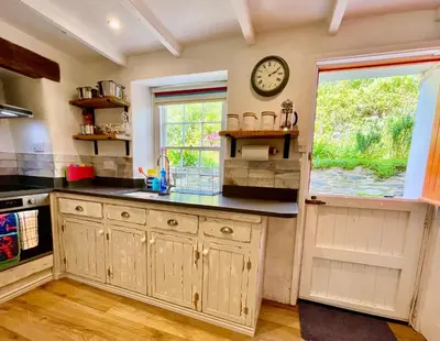 a kitchen with a clock on the wall and a window at Unique Retreat - 2 bedroom cliff top cottage with large terrace in Portloe