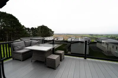 a patio with a couch and a table on a deck at ELITE BLUE LUXURY 3 BEDROOM LODGE NEWQUAY, CORNWALL in Newquay