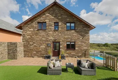 a stone house with two couches and a pool at Herons House Sleeps 12, heated Pool, hot tub, sauna, games room 5 Star! in Saint Columb Major