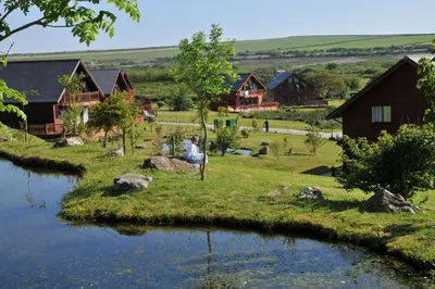 a person sitting on the grass next to a river at PointBreak Sleeps 12 with hot tub-Great celebration house-Dog friendly in Padstow