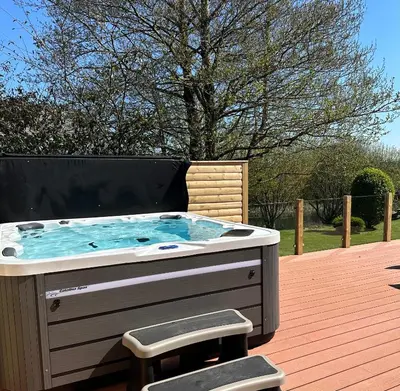 a hot tub sitting on a deck with two stools at Puffin Hot tub Lodge, 4 bedrooms Resort, Pool,Gym,Bar in Padstow