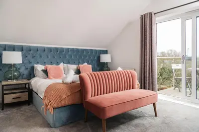 a bedroom with a bed and a chair and a window at Waveside-Waterside with hot tubResort PoolGym in Padstow