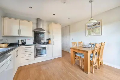 a kitchen with white cabinets and a wooden table at SandPipers Luxury hot tub lodge with 2 ensuites a private Sauna & BBQ terrace in Saint Columb Major