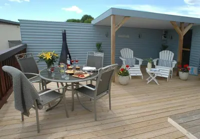 a patio with a table and chairs on a deck at SandPipers Luxury hot tub lodge with 2 ensuites a private Sauna & BBQ terrace in Saint Columb Major