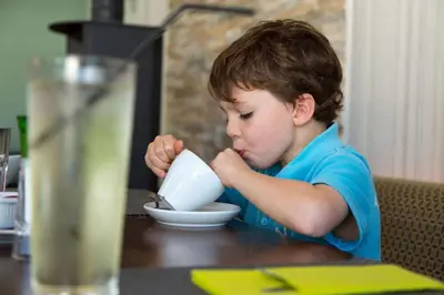 a young boy sitting at a table drinking from a bowl at Skylark sleeps 8 private Hot Tub & Dogs welcome Nr Padstow, Resort Pool Bar & Watersports in Saint Columb Major