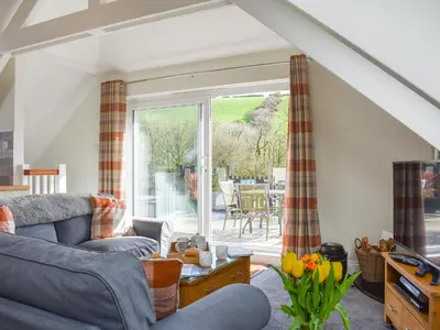 a living room with a couch and a sliding glass door at Camellia Cottage in Saint Ewe