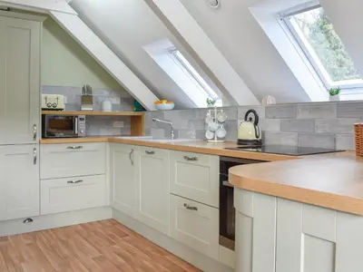 an attic kitchen with white cabinets and a sink at Camellia Cottage in Saint Ewe