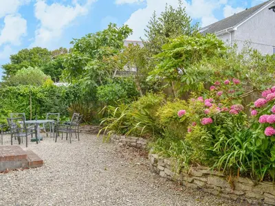 a garden with a table and chairs and flowers at Poppy Cottage in Crantock