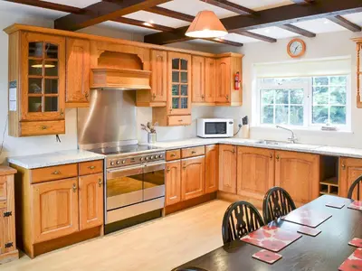 a kitchen with wooden cabinets and a table with a dining room at Poppy Cottage in Crantock