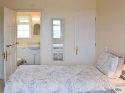 a white bedroom with a bed and a sink at Poppy Cottage in Crantock