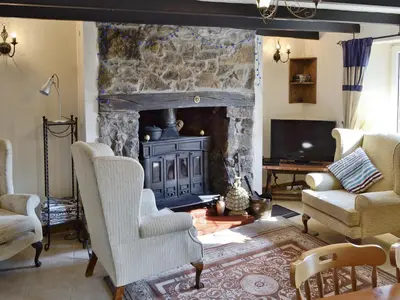 a living room with a stone fireplace and two chairs at Trecarne Cottage in Saint Cleer