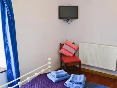 a bedroom with a bed and a tv and a chair at Trecarne Cottage in Saint Cleer