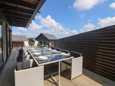 a patio with a table and chairs on a deck at Redwood, Retallack in Newquay