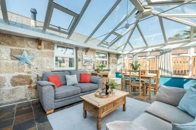 a conservatory with two couches and a table at Laity Vean Farmhouse and Hideaway in Carbis Bay