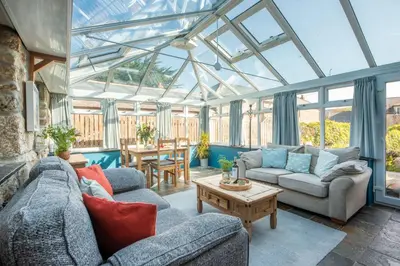 a living room with a conservatory with couches and a table at Laity Vean Farmhouse and Hideaway in Carbis Bay