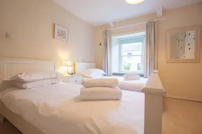 a bedroom with two beds with white sheets and a window at Gargoyle Cottage in St. Agnes
