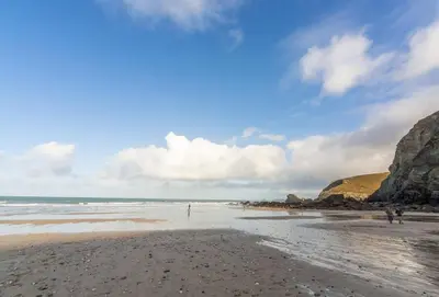 a beach with people walking on the sand and rocks at Gargoyle Cottage in St. Agnes