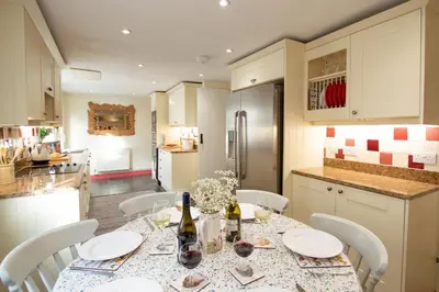 a kitchen with a table with white chairs and a kitchen with a refrigerator at Gargoyle Cottage in St. Agnes