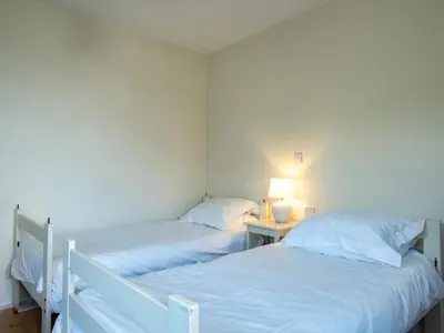 two beds in a small room with a table with a lamp at Croft Elms in Wadebridge