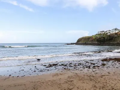 a beach with the ocean and a house in the background at EdyVean in St Austell