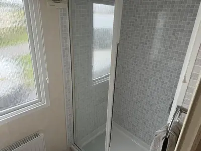 a glass shower door in a bathroom with a window at Bluebird K16 in St Merryn