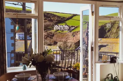 a table with a vase of flowers on a table in front of a window at Stowaway, Port Isaac Bay Holidays in Port Isaac