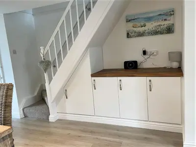a staircase with white cabinets in a living room at The Little Seahorse - Newly Renovated Cottage 5mins Walk The Beach with Hot Tub in Tywardreath