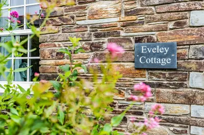 a sign on the side of a brick wall with flowers at Eveley Cottage in Boscastle