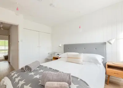a white bedroom with a large bed and a chair at Westward 8 in Polzeath