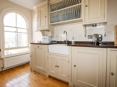 a kitchen with white cabinets and a window at Driftwood in Fowey