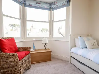 a bedroom with a bed and a chair and a window at Driftwood in Fowey