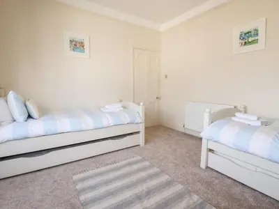 a bedroom with two beds and a rug at Driftwood in Fowey