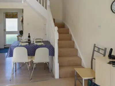 a dining room with a table and chairs and a staircase at Hazel Cottage in Budock Water