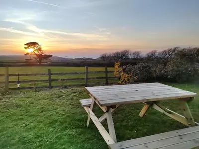 a wooden picnic table in a field with a fence at Trevose, sea views in Port Isaac