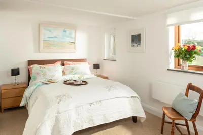 a white bedroom with a bed and a chair at The Hut in Bodmin