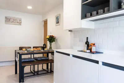 a kitchen with white cabinets and a table with wine bottles at Finest Retreats - Tinners Rest in St Austell