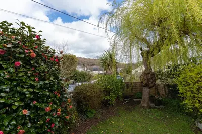 a garden with a hedge of roses and a tree at Finest Retreats - Tinners Rest in St Austell