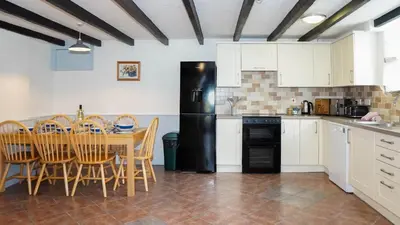 a kitchen with a table and a black refrigerator at Ta Mill Holiday Cottages & Lodges - Forge Cottage in Launceston