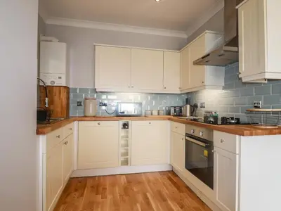 a kitchen with white cabinets and wooden floors at Flat 2 in Newquay