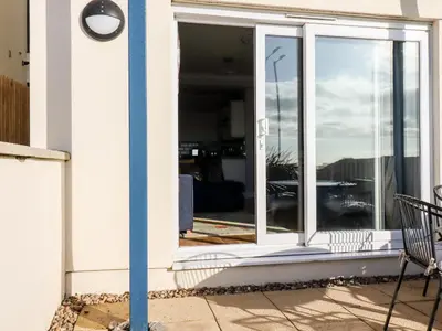 an open glass door on a house with a bench at Flat 2 in Newquay