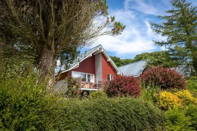 a red house with a balcony in a garden at Ta Mill Cottages & Lodges - Meadowview Chalet 1 in Launceston