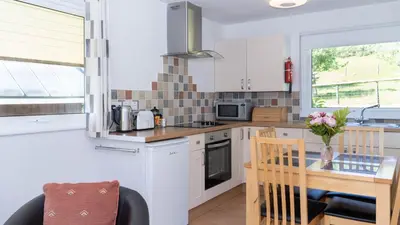 a kitchen with white cabinets and a table with a dining room at Ta Mill Cottages & Lodges - Meadowview Chalet 4 in Launceston