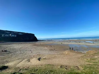 a beach with people on the sand and the ocean at Whispering Waves in Porthtowan, Beachfront Apartment in Porthtowan