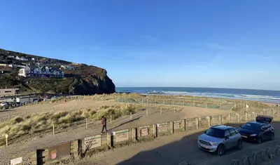 two cars parked on a road next to the beach at Whispering Waves in Porthtowan, Beachfront Apartment in Porthtowan