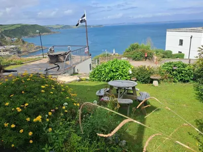 a garden with a table and chairs and the ocean at Eddystone Light Apartment in Mevagissey