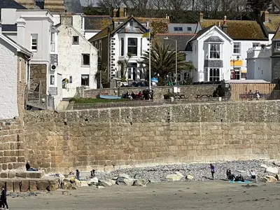 a group of people on the beach near a stone wall at Ocean Villas in Marazion