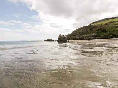 a beach with a body of water and a rocky shore at The Moonbeach Cabin in Gorran Haven