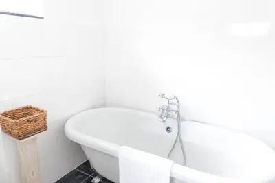 a white bath tub in a bathroom with a basket at Pollymoor Beach House in Holywell Bay